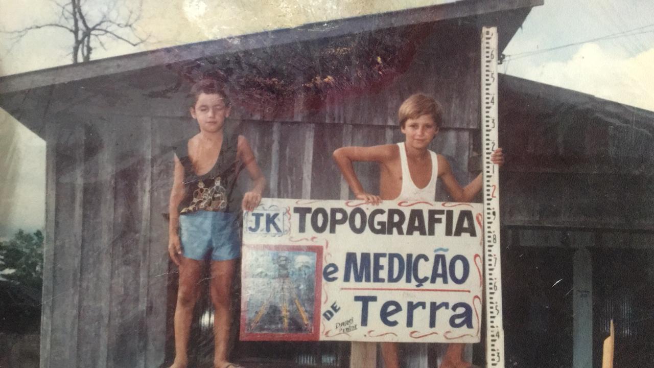 Zeique e o irmão, ainda crianças, segurando a placa da JK Topografia e Medição de Terra